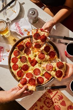 two people are grabbing slices of pizza from a pan with pepperoni and olives