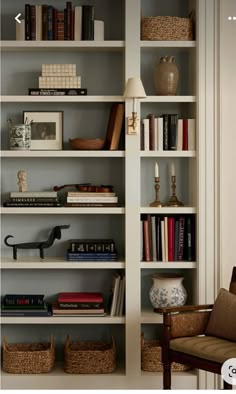 a book shelf filled with lots of books next to a chair and lamp on top of a hard wood floor