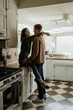 a man and woman standing in a kitchen next to an oven, looking at each other