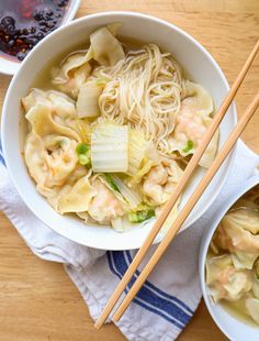 two bowls filled with noodles and vegetables next to chopsticks on a wooden table