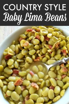 a bowl filled with beans and bacon next to a spoon on top of a table