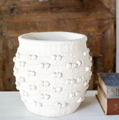 a white vase sitting on top of a table next to a book