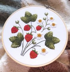 a close up of a embroidery on a piece of cloth with strawberries and daisies