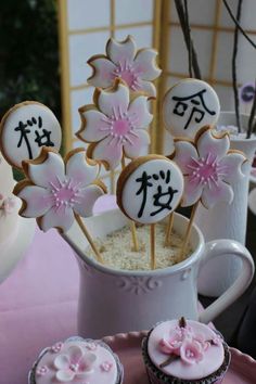 some cupcakes and cookies are in a vase on a table with pink flowers