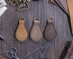 three leather key fobs sitting on top of a wooden table next to scissors