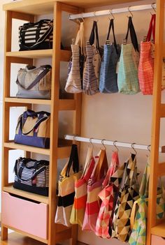 several purses and totes are hanging on the wall in front of a shelf