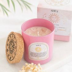 a pink candle next to a box of soap and some popcorn on a white surface