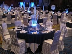 a banquet hall set up with white chairs and black table cloths, blue lights in the back