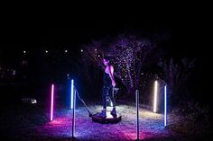 a man standing on top of a wooden platform surrounded by poles and lights in the dark