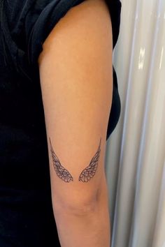 a woman's arm with an angel wing tattoo on the left side of her arm