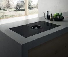 a kitchen counter with a black stove top next to a bowl of vegetables and utensils