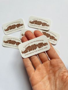 a hand holding four brown and white stickers with the words, i am the wilderness on them