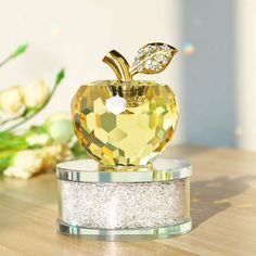 an apple shaped crystal object on top of a wooden table with flowers in the background