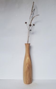 a wooden vase with dried flowers in it against a white wall, ready to be used as a decoration