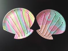 two paper plates shaped like fish on a black surface with one painted pink and the other green