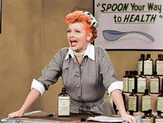 a woman sitting at a table with lots of bottles in front of her and an advertisement on the wall behind her