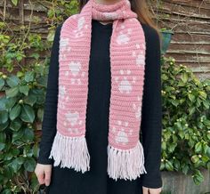 a woman wearing a pink knitted scarf with hearts on it and fringes around the edges