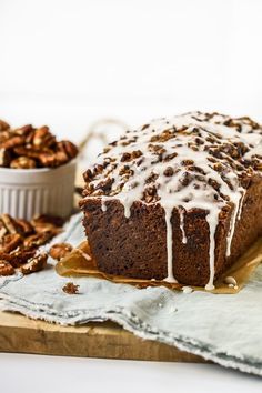 a loaf of cake sitting on top of a wooden cutting board next to some nuts