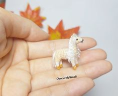 a tiny toy llama is being held in someone's hand with autumn leaves behind it