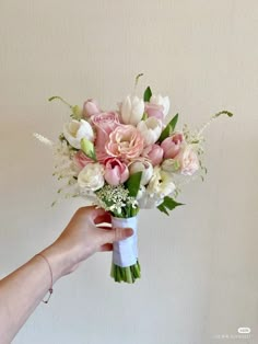 a hand holding a bouquet of pink and white flowers in it's left arm