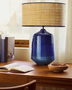 a blue vase sitting on top of a wooden desk next to a book and lamp