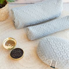 three decorative pillows on a table next to a bowl with black seeds and a gold spoon