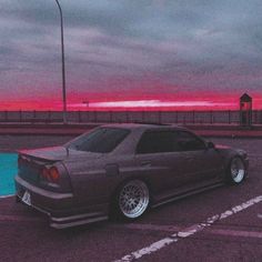 a car parked in a parking lot with the sun setting behind it and some clouds