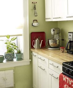 a kitchen with green walls, white cabinets and wooden counter tops in front of a window