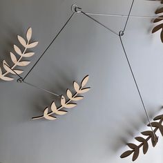 a metal sculpture with leaves hanging from it's sides on a gray wall next to a plant