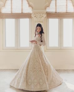 a woman in a white wedding dress looking at her cell phone while standing next to a window