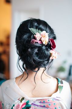 the back of a woman's head with flowers in her hair, wearing a floral dress