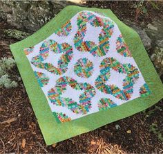 a green and white quilt sitting on top of a grass covered ground next to a tree