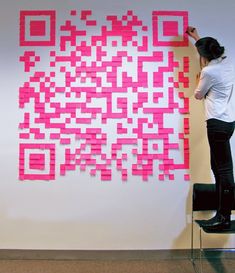 a woman standing on top of a stool next to a giant pink qr code