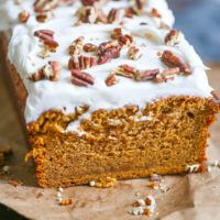 carrot cake with white frosting and pecans on top, sitting on a piece of parchment paper