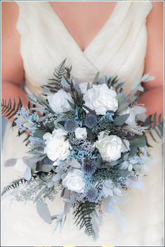 a bridal holding a bouquet of white and blue flowers in her hands with greenery