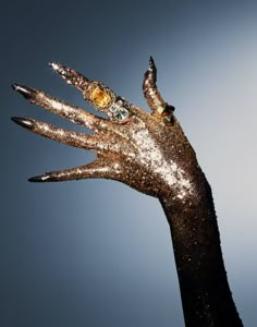 a person's hand with gold and silver glitter on it, against a blue sky