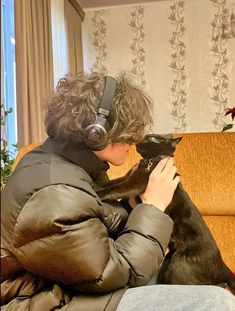 a woman sitting on a couch petting a black cat with headphones around her ears