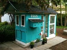 a small blue shed with the word eggs written on it's side and potted plants next to it