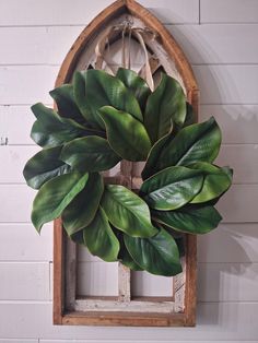 a large green leafy wreath hanging on the side of a white brick wall next to a window