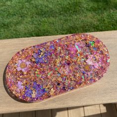 a wooden table with a piece of colorful rock on it's surface and grass in the background