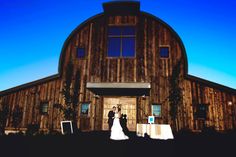 a bride and groom standing in front of a barn