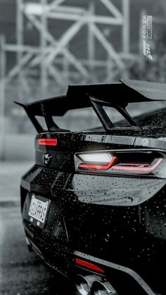 the back end of a black sports car with rain drops on it's hood