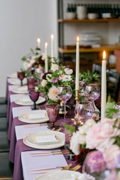 white, gold trimmed dishes placed on a royal purple table clothe with gold dinner ware. White tapered candles in gold candle holders and purple, white and pink flowered centerpieces are placed down the center of the table. Two types of purple glasses round out the table, lighter lavender tall stemware and shorter darker purple pedestal water glasses Purple And White Table Setting, Purple Table Scape, Purple And Pink Table Setting, Royal Table Setting, Purple Dinner Party Decor, Plum Table Setting, Eggplant Table Setting, Purple Dinner Party, Plum Wedding Decorations Table Settings