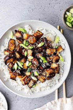 a white bowl filled with rice covered in tofu and sauce next to chopsticks