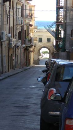 several cars parked on the side of a street next to tall buildings and an archway