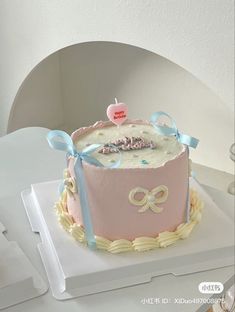 a pink and white birthday cake with blue ribbon around the edges on a table in a room