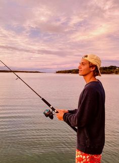 a man standing on the edge of a body of water while holding a fishing pole