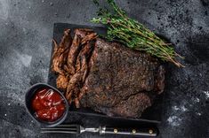 steak with sauce and herbs on black slate platter next to knife, fork and spoon