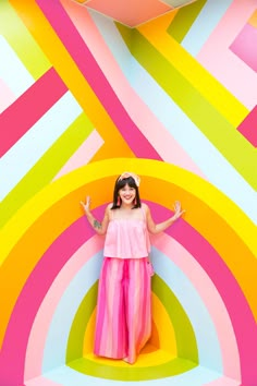 a woman standing in front of a multicolored wall with her arms out and hands up