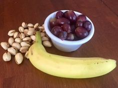 a banana, grapes and nuts are sitting on a wooden table next to a bowl